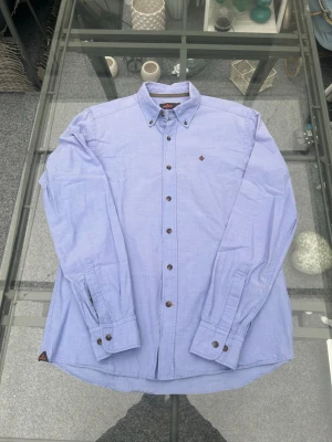 Morris skjorta L/41-42 – ljusblå sommar/preppy - Säljer en ljusblå Morris Oxfordskjorta i storlek L / 41-42. Perfekt till sommaren och enkel att styla till både shorts, jeans och linnebyxor. Clean preppy/old money-look med button down-krage och broderad logo.  Skön passform i 100% bomull och mycket bra skick. Funkar lika bra till vardag som till mer uppklädda fits.  • Storlek: L / 41-42 • 100% bomull • Ljusblå • Button down