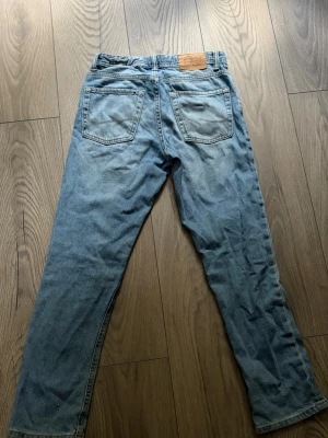 Ljusblå raka jeans från Jack n Jones  - Säljer ett par klassiska ljusblå jeans från jack n Jones raka ben och femficksmodell. Jeansen har en snygg tvätt och läderpatch med logga bak i midjan. Perfekta för en avslappnad och trendig stil.