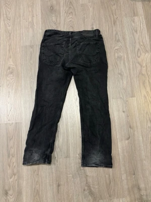 Svarta jeans från Jack & Jones - Säljer ett par svarta jeans från Jack & Jones med klassisk femficksdesign och raka ben. Jeansen har en snygg tvättad look och är tillverkade i jeansmaterial. Perfekta för en avslappnad stil.