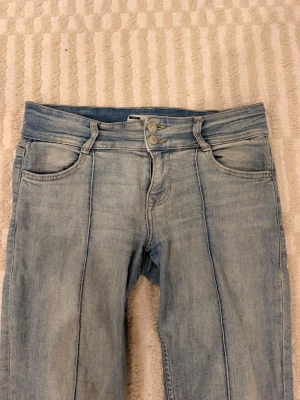 Bootcut jeans från Bershka ljusblå - Bootcut jeans från Bershka i ljusblå tvätt med klassisk femficksdesign och dubbla silverfärgade knappar i midjan. Jeansen har markerade sömmar längs benen och är tillverkade i jeansmaterial. 