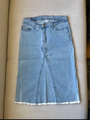 Vintage dtn Ljusblå Jeanskjol Stl 36 – Y2K Low Waist Stretch - Säljer en riktigt snygg vintage jeanskjol från dtn (Dalton Company) i en härlig ljusblå färg. Denna vintagepärla har den helt rätta Y2K-looken med low waist-passform och fransad råkant nedtill. Tack vare stretchen sitter den väldigt bekvämt.   • Storlek: 36 • Material: 98% Bomull, 2% Lycra • Detaljer: 5 fickor och slits bak (24 cm) • Skick: Gott skick   Mått (platt): • Midja: ca 35 cm (omkrets 70 cm) • Längd: 62 cm