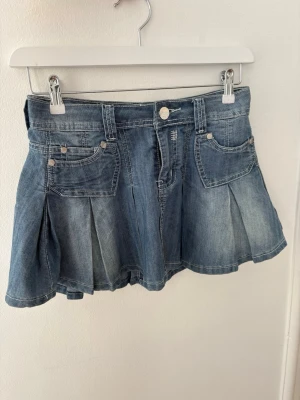 Blå jeanskjol med fickor och veck - Snygg blå jeanskjol med klassiska fickor fram och bak samt markerade veck. 
