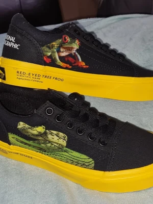 VANS National Geographic sneakers Nya stl 28 - Unika barn sneakers med gula sulor från Vans National Geographic stl 28.Skorna har coola tryck av grodor på sidorna och tydliga loggor. Materialet är canvas och detaljerna är i starka färger som verkligen sticker ut. Perfekta för dig som vill ha något annorlunda och djurinspirerat.