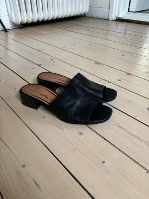 Tamaris sandaler med klack i storlek 38 - Ett par svarta mules med en öppen tå och en blockklack. Skorna har en slät ovandel och en bekväm passform. 
