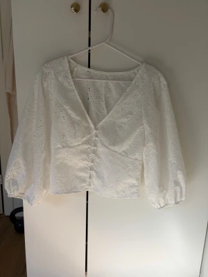 Vit blus med puffärm - Söt vit blus med broderade blommor och v-ringning. Blusen har puffiga långärmar med resår vid ärmslut och knäppning framtill. Köpt på Plick 