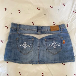Blå jeanskjol - Snygg blå mini jeanskjol med broderade bakfickor. Storlek 32. Mått rakt ner: ca 29 Midjemått: ca 88 