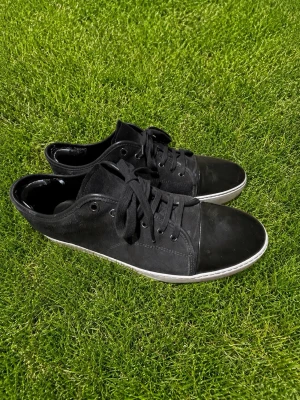 Svarta låga sneakers med vit sula - Stilrena svarta sneakers med lågt skaft och klassisk vit sula. Skorna har svarta skosnören, metallöljetter och en tådel i blankare material som ger en snygg kontrast. Perfekta för en clean och urban look. grön/gråa