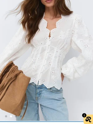 Vit broderad blus från River Island - Snygg vit blus från Gina med broderade blommor och hålmönster. Blusen har långärmade puffärmar, knappar framtill och en scallopad kant vid nederdelen. Materialet är lätt och luftigt, perfekt för en trendig look. Aldrig använt den kan tyvärr ej lämna tillbaks den för tiden är slut, för liten 