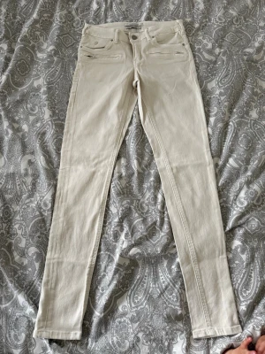 Beiga skinny jeans med dragkedjor Maison scotch - Snygga beiga skinny jeans med två dragkedjor framtill och klassisk femficksdesign. Hög midja och smal passform som sitter tajt längs benen. Perfekta för en stilren och trendig look.