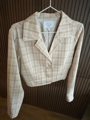Beige rutig kavaj från NA-KD  - Stilren beige kavaj med rutigt mönster. Kavajen har klassisk krage, tre knappar framtill och är croppad i modellen. Storlek M