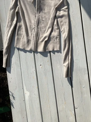 Beige  zip-hoodie med huva - En basic beige  hoodie med dragkedja och huva. Tröjan har dragsko vid huvan och är tillverkad i ett mjukt, bekvämt material. Perfekt för en avslappnad stil och enkel att matcha med andra plagg.