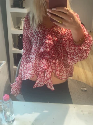 Rödvit blommig volangblus - Snygg blus från Zara med rödvitt blommönster och volangdetaljer framtill. Lätt transparent material och långa ärmar med lös passform.