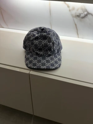 Gucci denimkeps med monogram - Snygg keps från Gucci i blå denim med klassiskt GG-monogram över hela kepsen. Böjd skärm och justerbar baksida. Perfekt accessoar för att lyfta din streetwear-look.