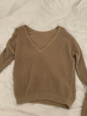 Beige stickad tröja från NA-KD - Snygg beige stickad tröja från NA-KD med djup V-ringning och ribbade muddar. Tröjan har en avslappnad passform och är perfekt för lager-på-lager. Tillverkad i mjukt stickat material som känns skönt mot huden.