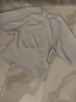 Vit t-shirt från pull&bear - Säljer en vit t-shirt från pull&bear med breda, korta ärmar och rund halsringning. T-shirten har en enkel och clean design, perfekt för en avslappnad stil. Tillverkad i mjuk bomull för extra komfort.
