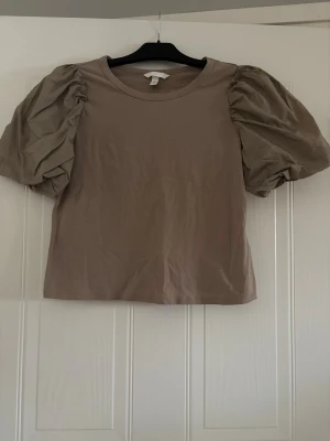 Beige topp med puffärmar från H&M - Supersnygg beige topp från H&M med trendiga puffärmar och rund halsringning. Toppen är i mjuk bomull och har en rak passform som passar perfekt till både jeans och kjol. Enkel men ändå unik med sina voluminösa ärmar.