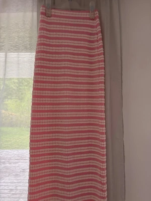 Rosa och vit randig långkjol - Snygg långkjol med rosa och vita ränder i ett stickat material. Kjolen har en rak passform och känns både trendig och bekväm. Perfekt för dig som gillar en färgglad och lekfull stil. Jag är ca 172 om någon undrar över längden på kjolen.
