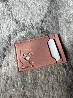 Rosa korthållare Hero's ID - Säljer en rosa korthållare i slät konstläder med ett coolt superhjälte-motiv präglat på framsidan. Perfekt för att hålla koll på dina kort och ID. Slimmad och smidig design som enkelt får plats i fickan.
