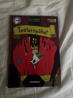 Teaterspöket av Wänblad & Forshed - En färgglad och rolig barnbok med titeln 'Teaterspöket', skriven av Mats Wänblad och illustrerad av Pelle Forshed. Omslaget är mörkrött med teatermotiv och tecknade figurer, tryckt i hårdpärm. Perfekt för dig som gillar spännande och humoristiska berättelser.