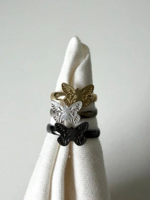 Ringar med fjäril i guld, silver, svart - Tre stilrena ringar med fjärilsdetaljer i metall – en i guld, en i silver och en i svart. Justerbara i storlek 🤍 söta att ha i stack 
