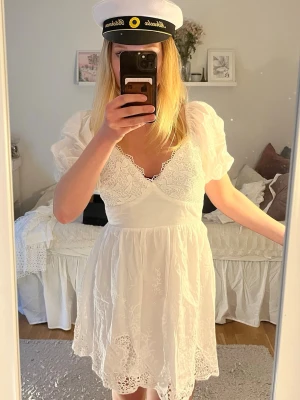 Studentklänning - Superfin vit kort klänning med spetsdetaljer och puffärmar. Klänningen har v-ringning och broderade detaljer på kjolen. Perfekt för student eller sommarens alla tillfällen.