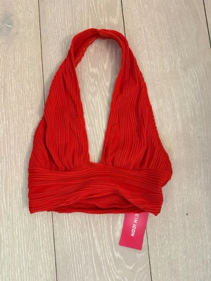 Röd halterneck topp från NLY ICON - Snygg röd halterneck topp från NLY ICON med ribbad struktur och bred resår under bysten. Toppen är ärmlös och croppad, perfekt för att skapa en trendig look. Passar till både jeans och kjol för en cool stil.