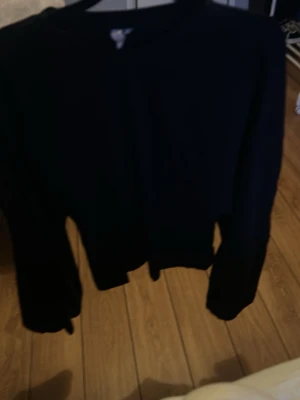 Svart basic cardigan - En enkel svart cardigan med långa ärmar och rund hals. Perfekt att slänga över en t-shirt eller linne. Klassisk modell utan synliga detaljer eller mönster, vilket gör den lätt att matcha med olika outfits.