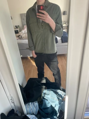 Olivgrön overshirt  - Säljer en stilren olivgrön overshirt från Weekday. Skjortjackan har två stora bröstfickor med lock, knäppning framtill och klassisk krage. Tillverkad i ett mjukt bomullstyg som ger en avslappnad look. Perfekt att bära öppen eller stängd över en t-shirt.