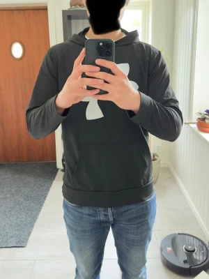 Under Armour hoodie svart strl M - Svart hoodie från Under Armour med stor logo framtill. Lätt och bekvämt funktionsmaterial som passar perfekt till både träning och vardag. Storlek XL men sitter mer som M på grund av modellen/passformen. Bra skick.  Modellen på bilden är ca 185 cm lång och väger ca 78 kg för referens.