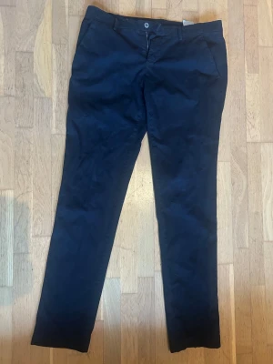 Mörkblå Mason Chinos med rak passform - Snygga italiensktköpta mörkblå chinos med rak passform och klassisk design. Byxorna har sidofickor och bälteshällor i midjan. Tillverkade i ett mjukt bomullsmaterial som ger en skön känsla. Perfekta för dig som gillar en clean och stilren look.
