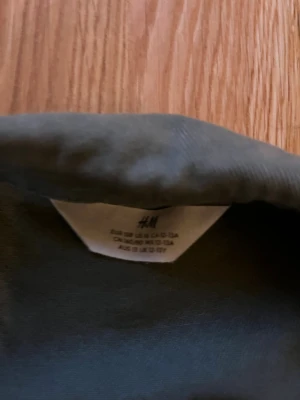 Olivgrön jacka från H&M - Snygg olivgrön jacka från H&M med klassisk krage och raka sömmar. Jackan har långa ärmar och är tillverkad i ett mjukt bomullstyg. Perfekt för dig som gillar en stilren och enkel look.