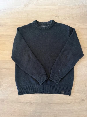 Svart stickad tröja från Pull&bear - Klassisk svart stickad tröja från Pull&bear med rund halsringning och ribbade muddar vid ärmslut och nederkant. Perfekt basplagg i garderoben med enkel och stilren design. Materialet känns mjukt och passar bra till lager på lager.