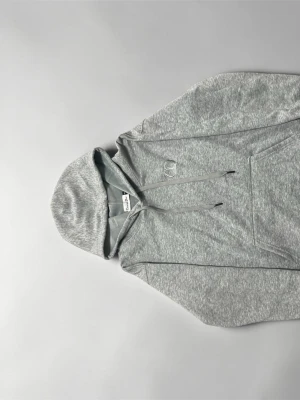 Grå broderad hoodie - Storlek S - Snygg grå hoodie från Champion med klassisk logga broderad på bröstet. Hoodien har dragsko i huvan och en stor magficka framtill. Tillverkad i mjuk bomullsblandning som är perfekt för en chill och avslappnad stil.