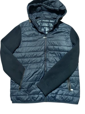 Mörkblå Massimo Dutti pufferjacka med huva - Snygg mörkblå Massimo Dutti pufferjacka med quiltad front och rygg, stickade ärmar och praktisk huva. Jackan har dragkedja framtill och två sidofickor med dragkedja. Perfekt för kalla dagar och ger en modern look.