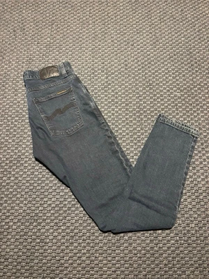 Mörkblå jeans från Nudie Jeans 29/32 - Snygga mörkblå jeans från Nudie Jeans med klassisk modell och diskret broderad bakficka. Jeansen har raka ben och är tillverkade i mjukt denimtyg som sitter skönt hela dagen. Perfekta för dig som gillar stilrena och tidlösa jeans. ‼️OBS‼️ jeansen ser mörkare ut på bilden en vad de är. Tveka inte o höra av dig vid funderingar