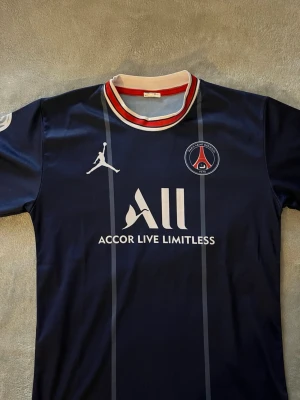PSG Neymar Jr matchtröja blå - Snygg blå PSG matchtröja med Neymar Jr och nummer 10 på ryggen. Tröjan har vita och röda detaljer vid kragen, PSG-logga på bröstet och Jordan-logga. Tillverkad i lätt och ventilerande material, perfekt för fotboll eller träning.
