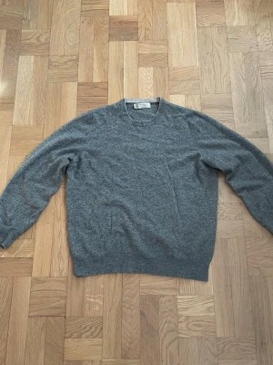 Brunello Cucinelli Cashmere Tröja - Mjuk och lyxig grå stickad tröja från Brunello Cucinelli i cashmere. Klassisk rund halsringning och ribbade muddar vid ärmslut och nederkant. Perfekt för dig som gillar stilrena och exklusiva plagg. Storlek 50 sitter som small