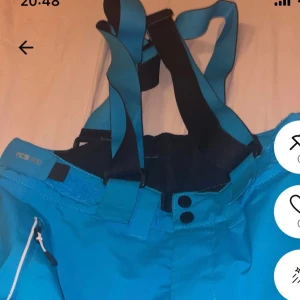 Blå täckbyxor med hängslen Everest - Säljer ett par blå täckbyxor från Everest med justerbara svarta hängslen och dragkedja i sidan. Byxorna har en sportig look och är perfekta för vinterns alla äventyr. Materialet är slitstarkt och vattenavvisande, med logga på benet.