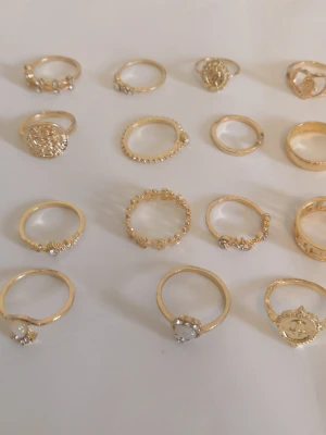 15-pack guldfärgade ringar  - 15 st  guldfärgade ringar med olika former och mönster. Materialet är zinc alloy + rhinestones + resin (#299)