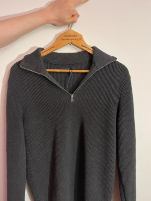 Mörkgrå stickad tröja från Riley - Snygg mörkgrå stickad tröja från Riley med ribbad struktur och halvzip-dragkedja framtill.  Ny med prislapp! Säljer pga fel storlek. Skriv vid bild med tröja på!