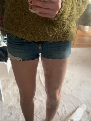 Blå jeansshorts med spetsdetalj - Säljer ett par blå denimshorts med råa kanter och vit spetsdetalj på ena sidan. Shortsen har dragkedja framtill och klassiska bakfickor. Perfekta för sommaren. Säljer för 130 men kan absolut diskutera priset. Dessa är för små för mig, är 167 cm. Skriv privat om frågor 
