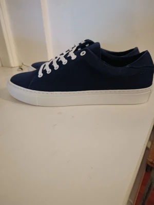Mörkblå canvas sneakers med vit sula - Stilrena mörkblå sneakers i canvas med vita snören och vit, platt sula. Klassisk låg modell som passar till det mesta och ger en clean look. Perfekta för dig som gillar enkel och snygg design.