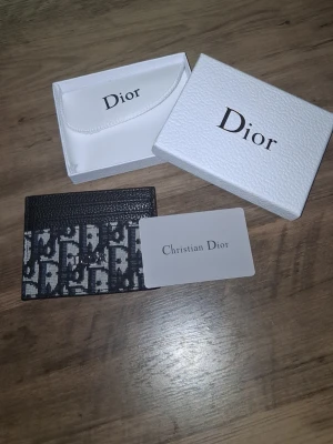 Dior svart kortfodral i canvas - Snyggt svart kortfodral från Dior med ikoniskt monogrammönster i vitt och grått. Tillverkat i tålig canvas med detaljer i läder. Kommer med original ask och kort. Perfekt för dig som vill ha en stilren och lyxig accessoar i fickan.