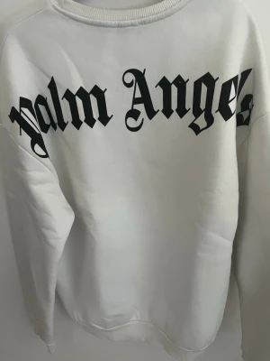 Vit sweatshirt från Palm Angels - Vit sweatshirt från Palm Angels med stor svart logga i font över ryggen och mindre logga framtill. Klassisk rund halsringning och ribbade muddar.