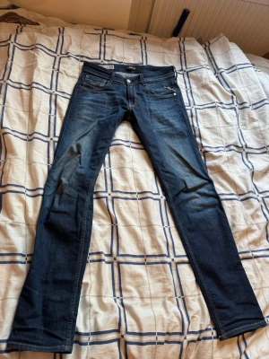 Mörkblå slim fit jeans från Replay - Snygga mörkblå slim fit jeans från Replay, modell Anbass. Jeansen har klassisk femficksdesign, diskreta slitningar och kontrastsömmar. Perfekta för dig som gillar en smal siluett och tidlös stil. Materialet är mjukt denim med lite stretch för extra komfort.