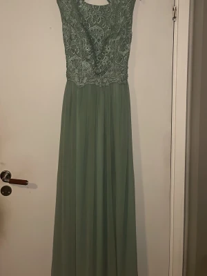 Grön långklänning med spetsdetaljer - Elegant grön långklänning med vackert spetsliv och öppen rygg. Kjolen är i ett tunt, flytande material och klänningen har breda axelband. Perfekt för speciella tillfällen där du vill känna dig extra fin. Skulle säga att den passar 36/38. Vet du med att du är bredaxlad/större byst, är denna klänning ej för dig tyvärr. Är pga detta jag säljer den