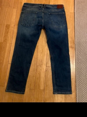 Mörkblå raka jeans från Pepe jeans - Säljer ett par mörkblå raka jeans från Pepe Jeans med klassisk femficksdesign och läderpatch bak i midjan. Jeansen har en snygg tvätt och raka ben som ger en avslappnad look. Perfekta till en streetwear-outfit eller casual stil.
