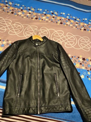 Svart skinnjacka Jack & Jones Core - Snygg svart skinnjacka från Jack & Jones Core med ståkrage och dragkedja framtill. Jackan har quiltade detaljer på axlarna och två fickor med dragkedja. Perfekt för en cool och stilren look.