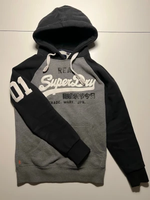 Superdry hoodie - svart/grå - size M - Hejsan! Säljer denna as mjuka hoodien från Superdry! Perfekt nu när våren långsamt närmar sig. Storlek M, skicket är super bra likaså priset, som går att diskutera. Vid fler frågor är det bara att skriva!  MVH VMresell