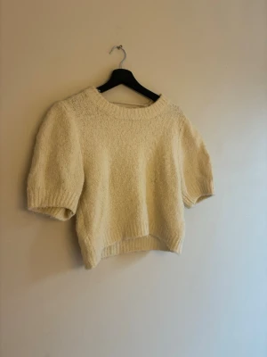 Vit stickad tröja med puffärm - Kort, vit stickad tröja med rund hals och puffiga, halvlånga ärmar. Tröjan har ribbstickade muddar vid ärmslut och nederkant. Perfekt för lager på lager och en avslappnad stil.